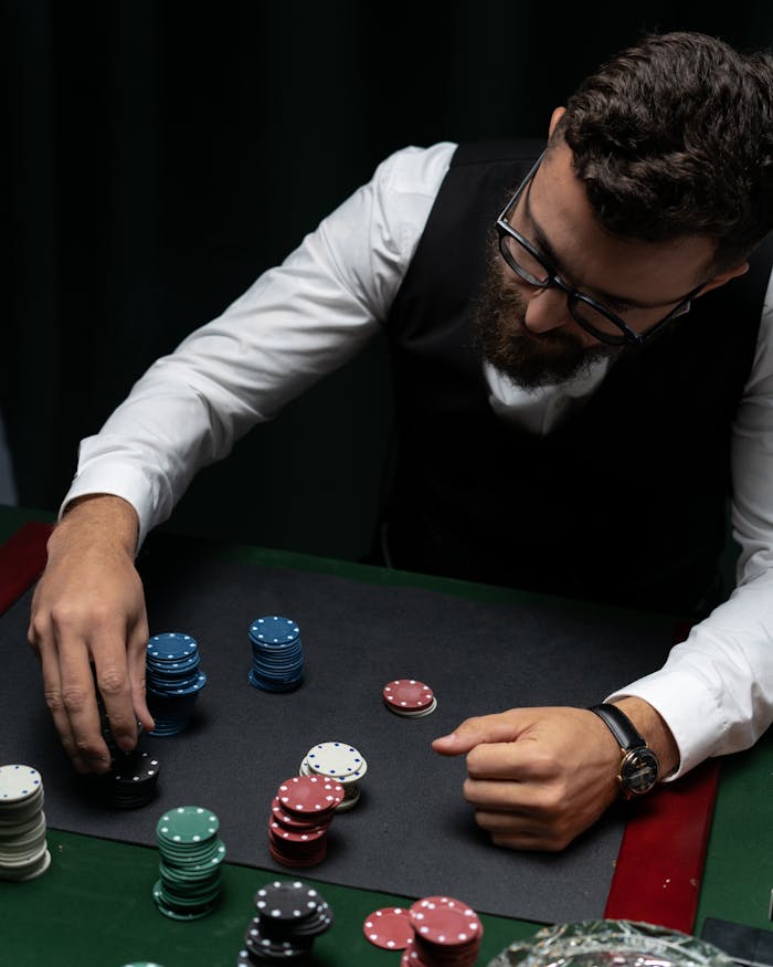 Bearded man in vest stacking poker chips at a casino table from above, focused and strategic.